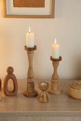 Stylish candlesticks with burning candles and other decor on cabinet near beige wall indoors