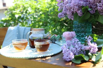 Beautiful lilac flowers, sweets and tea on wooden table in garden