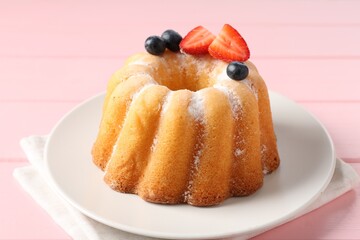 Tasty Bundt cake with powdered sugar and berries on pink wooden table, closeup