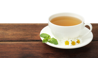 Delicious chamomile tea in cup, fresh flowers and mint on wooden table against white background