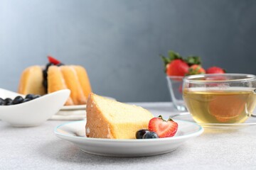 Piece of tasty bundt cake with berries and tea on light grey table, closeup