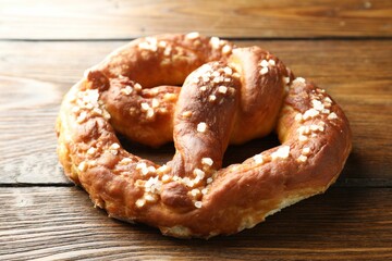 Tasty pretzel with salt on wooden table, closeup