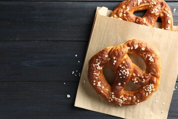 Tasty pretzels with salt on dark wooden table, top view. Space for text