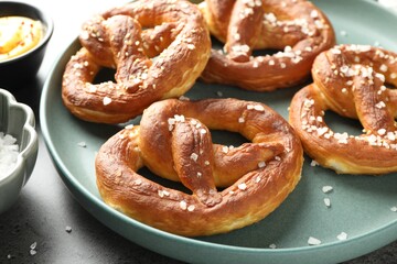Tasty pretzels with salt and sauce on grey table, closeup