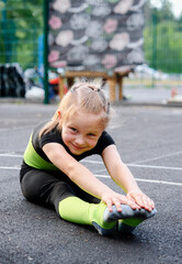 Sports and healthy childhood. Little girl does acrobatics and stretching exercises on playground in...