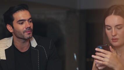 Portrait of focus beautiful woman talking with couple while looking at smartphone with serious face at bar. Capturing natural face beauty with dressing up social interaction at night club. Vinosity.