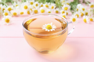 Delicious chamomile tea in glass cup and fresh flowers on pink wooden table, closeup