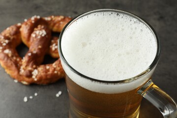 Glass of beer and tasty pretzel on dark textured table, selective focus