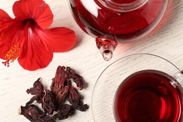 Delicious hibiscus tea in glass cup, teapot, dry roselle sepals and flower on light wooden table, flat lay © New Africa