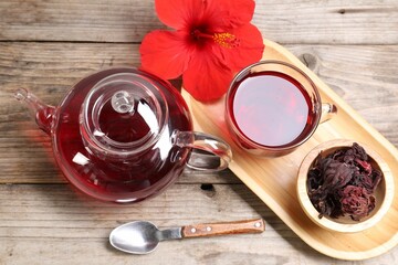 Delicious hibiscus tea in glass cup, teapot, dry roselle sepals and flower on wooden table, above view