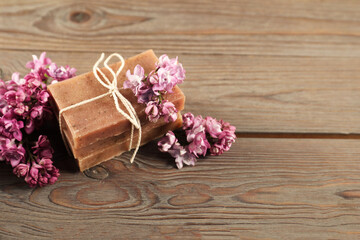 Fototapeta premium Soap bars and lilac flowers on wooden table, closeup. Space for text