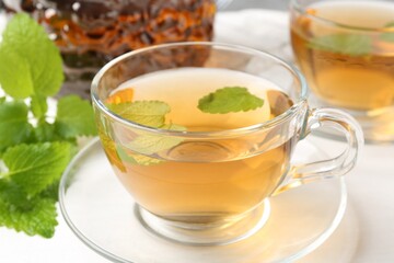 Aromatic lemon balm tea in glass cups, teapot and fresh leaves on white table, closeup