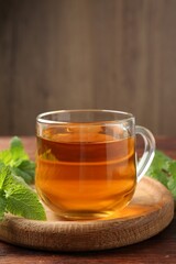 Aromatic lemon balm tea in glass cup and fresh leaves on wooden table