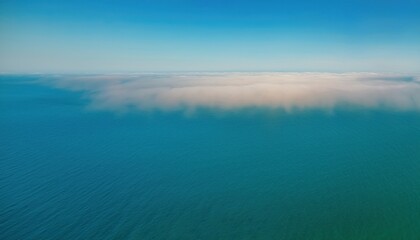 Fototapeta premium aerial view of ocean surface blending into low coastal fog under clear blue sky for web design, nature branding, environmental print, minimalist background or atmospheric editorial layout