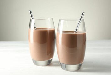 Tasty chocolate milk in glasses on white wooden table, closeup