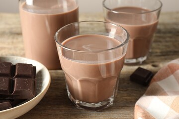 Tasty chocolate milk in glasses and pieces on wooden table, closeup