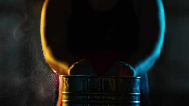 Close-up: Hands clap, creating a cloud of chalk over a metal container. Dramatic yellow and blue rim lighting highlights slow-motion particle dispersion.