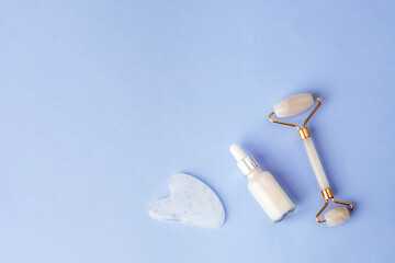 Facial skincare tools and serum bottle on pastel blue background, flat lay composition for beauty and wellness theme. Top view, copy space