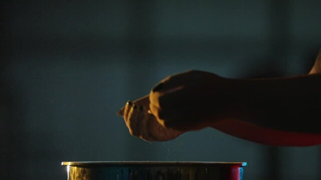 Close-up: Hands clap, creating a cloud of chalk over a metal container. Dramatic yellow and blue rim lighting highlights slow-motion particle dispersion.