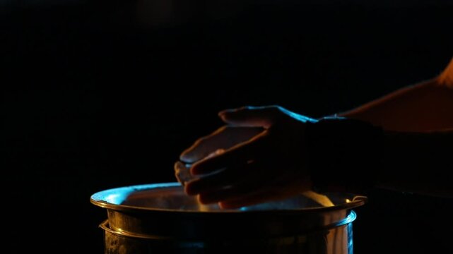 Close-up: Hands clap, creating a cloud of chalk over a metal container. Dramatic yellow and blue rim lighting highlights slow-motion particle dispersion.