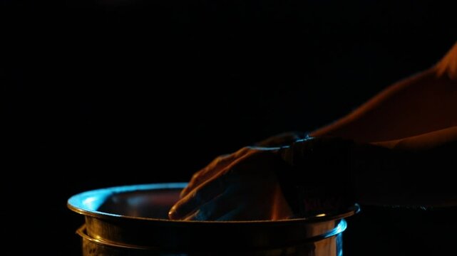 Close-up: Hands clap, creating a cloud of chalk over a metal container. Dramatic yellow and blue rim lighting highlights slow-motion particle dispersion.