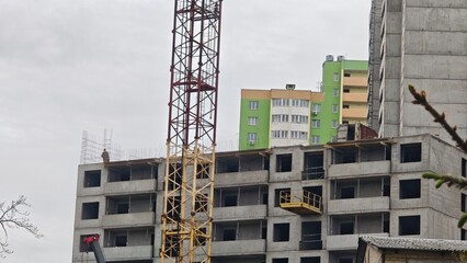 Multi-story concrete building under construction with a crane and scaffolding in urban area. Concept of urban development, construction process and industrial progress © Olena