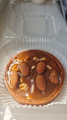 Caramel tart topped with whole almonds and walnuts in a clear plastic container. Concept of sweet indulgence, dessert treat and artisanal pastry