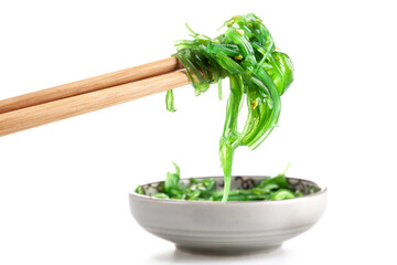 Chopsticks holding Japanese seaweed salad. Japanese cuisine - Wakame salad, Chuka seaweed salad isolated on a white background.