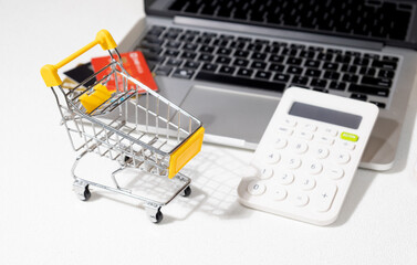 Online Shopping Concept with Empty Miniature Cart and Laptop on Desk