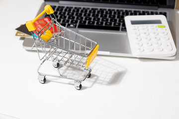 Online Shopping Concept with Empty Miniature Cart and Laptop on Desk