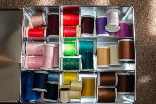 Caja met&aacute;lica que contiene varios hilos de costura de distintos colores, organizados dentro del recipiente. Los carretes de hilo, utilizados para coser y reparar prendas, reflejan un ambiente de traba