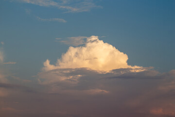 A striking cumulonimbus cloud stands prominently in a sky transitioning from blue to soft pink hues...