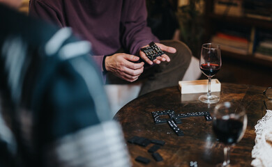 An intimate evening scene featuring friends enjoying a game of dominoes with glasses of red wine on a cozy wooden table in a living room setting.