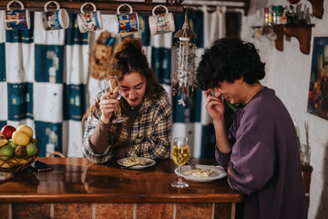 Two young friends share laughter and joy while dining and enjoying wine in a charming bar. Capturing the essence of camaraderie, happiness, and relaxation in a warm and inviting indoor space.