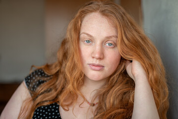 Fototapeta premium A natural and expressive close-up portrait of a woman with red hair and green eyes radiating authenticity and confidence, with atmospheric lighting adding warmth and character to the image.