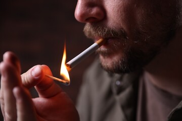 Fototapeta premium Man lighting cigarette with match on blurred background, closeup