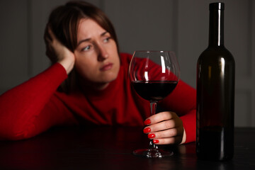 Alcohol addiction. Woman with glass of red wine and bottle at wooden table indoors, selective focus