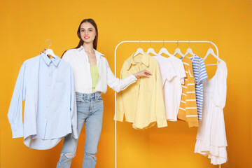 Smiling fashion stylist and rack with clothes on yellow background