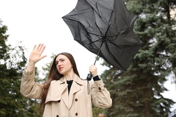 Woman with broken umbrella fighting wind outdoors, low angle view