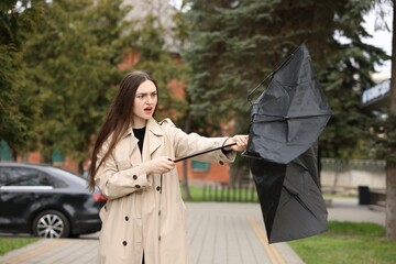 Woman with broken umbrella fighting wind outdoors