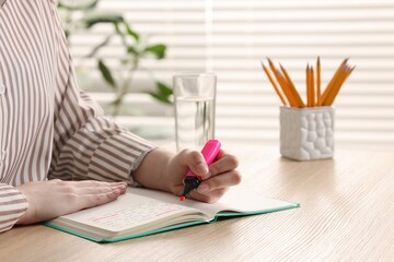 Woman highlighting important information at wooden desk indoors, closeup