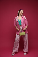 Fototapeta na wymiar Fashionable full-length portrait of beautiful woman in stylish outfit on dark red background