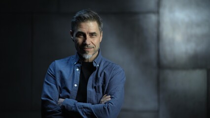Portrait of happy mature casual man, smiling, standing in front of dark loft wall. Older, middle aged, mid adult, man in his 40s or 50s in shirt.