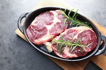 Pieces of raw beef meat and spices in baking dish on gray textured table, top view