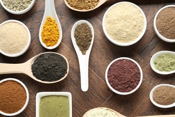 Different superfood powders in bowls and spoons on wooden table, flat lay