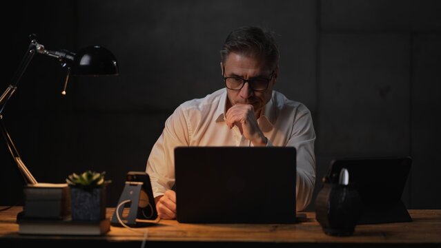 Businessman sitting at desk with laptop computer. Entrepreneur working late in office. Older, middle aged, mid adult, man in his 40s or 50s in business casual.