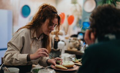 An attentive young woman carefully prepares food at a bar, engaging with a friend in a cozy ambiance.