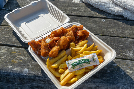 Fish and chips in a takeout container with fritessaus on a wooden surface, ready to be enjoyed outdoors. Katwijk aan Zee, the Netherlands. 2 May 2025.
