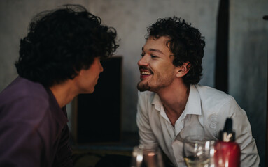 Two friends share an engaging moment in a relaxed indoor setting, laughing cheerfully. The casual ambiance and natural interaction depict a genuine bond and the joy of heartfelt conversations.