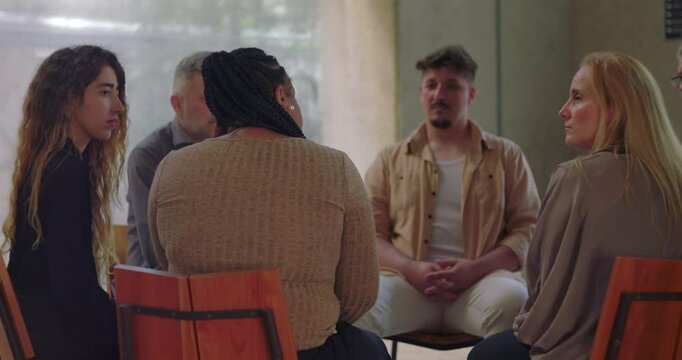 Woman engaging with peers in emotional group discussion, therapy participants gathered in circle for mutual support and healing